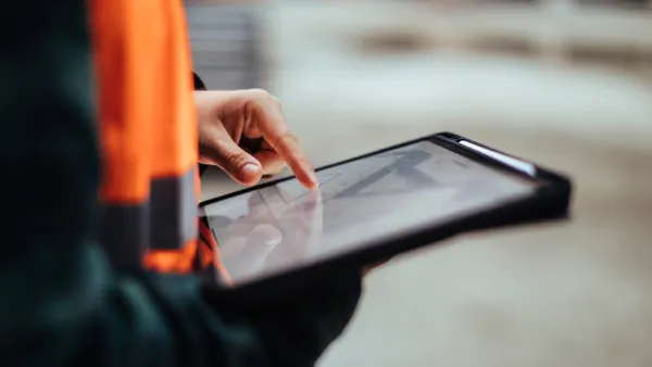 A person with a safety vest uses an electronic tablet.