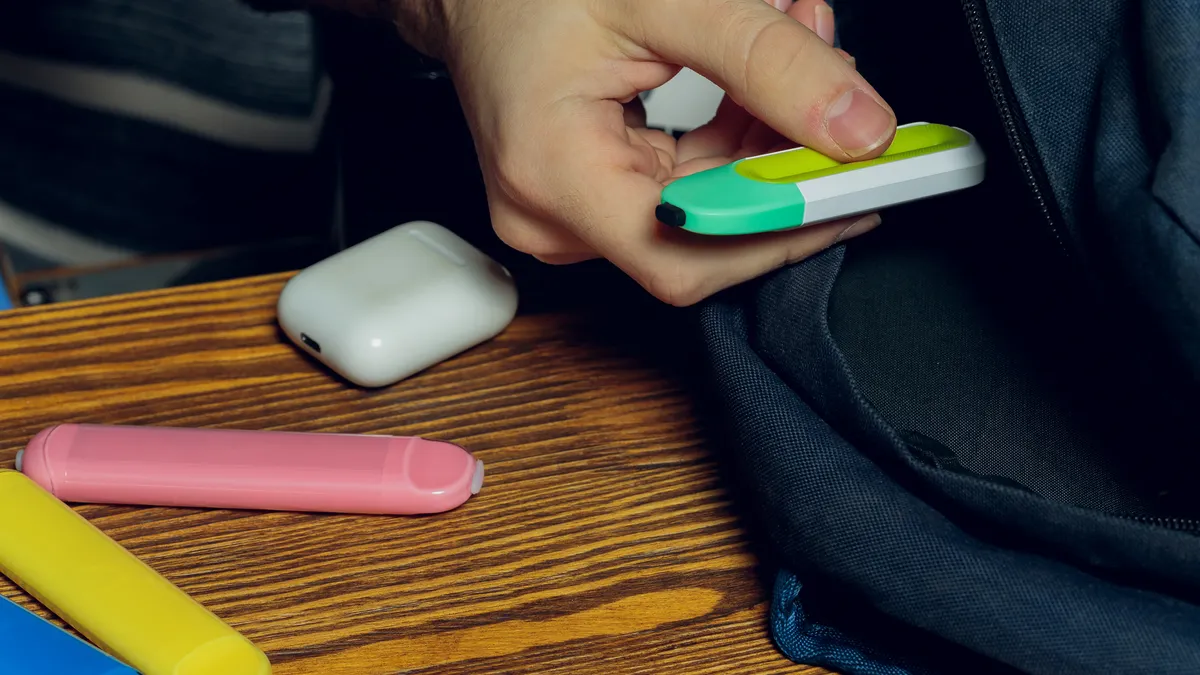 A vape POD e-cigarette or nicotine vapor stick by school bag.