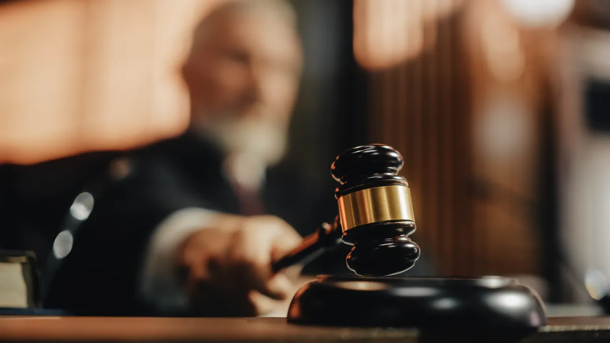 Judge blurred in the background strikes brown gavel on court bench.