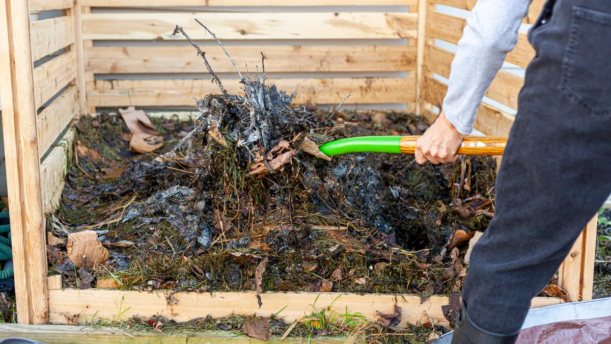 A gardener shovels partially composted yard material from a heap onto tarp for aeration.