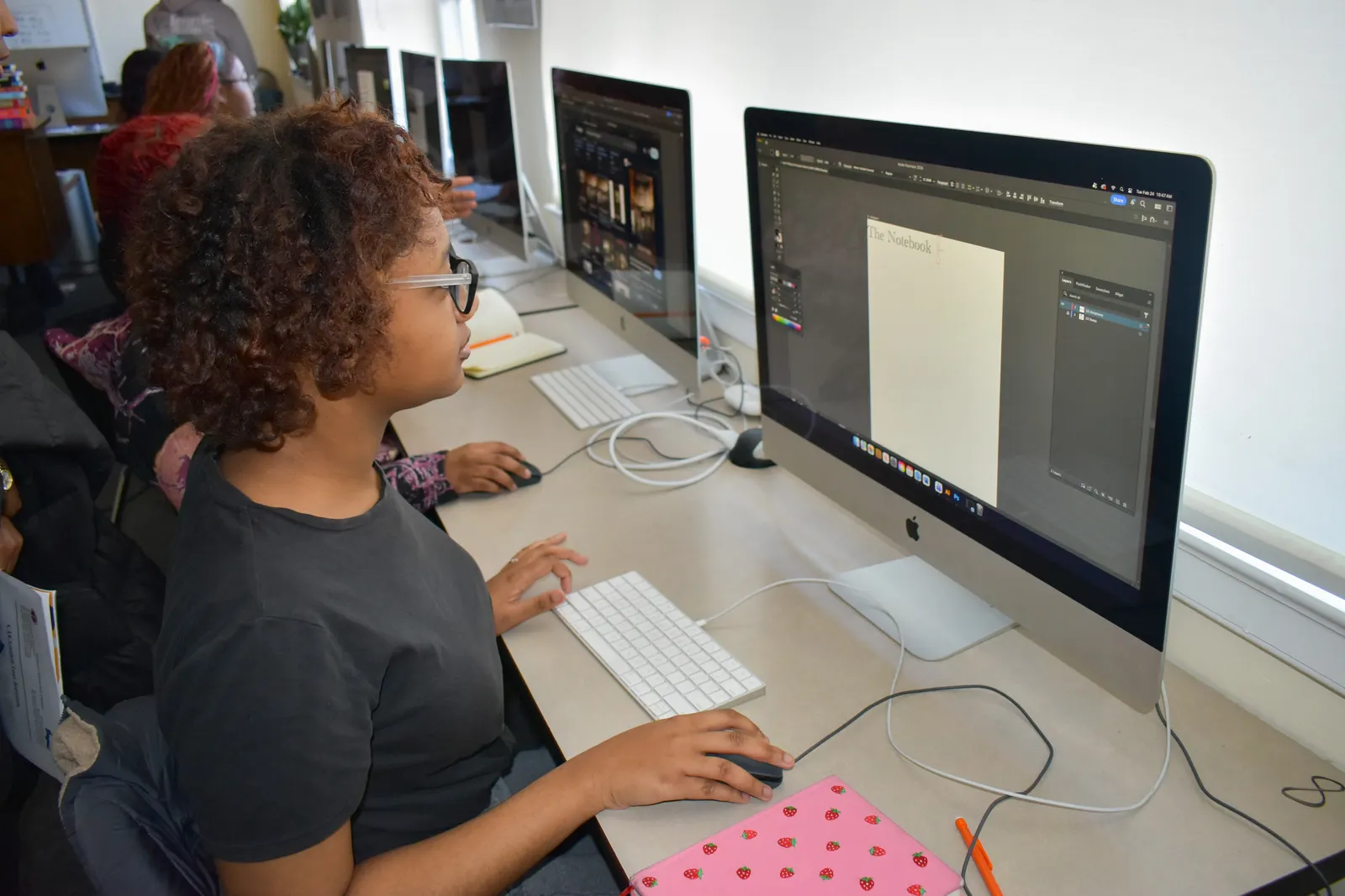 A student sits at a desk in a classroom and is looking at a computer monitor.