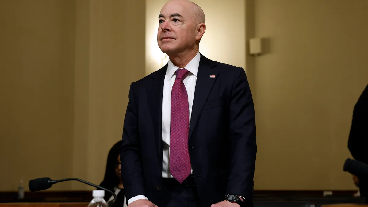 A man in a suit stands behind a chair while holding its back.