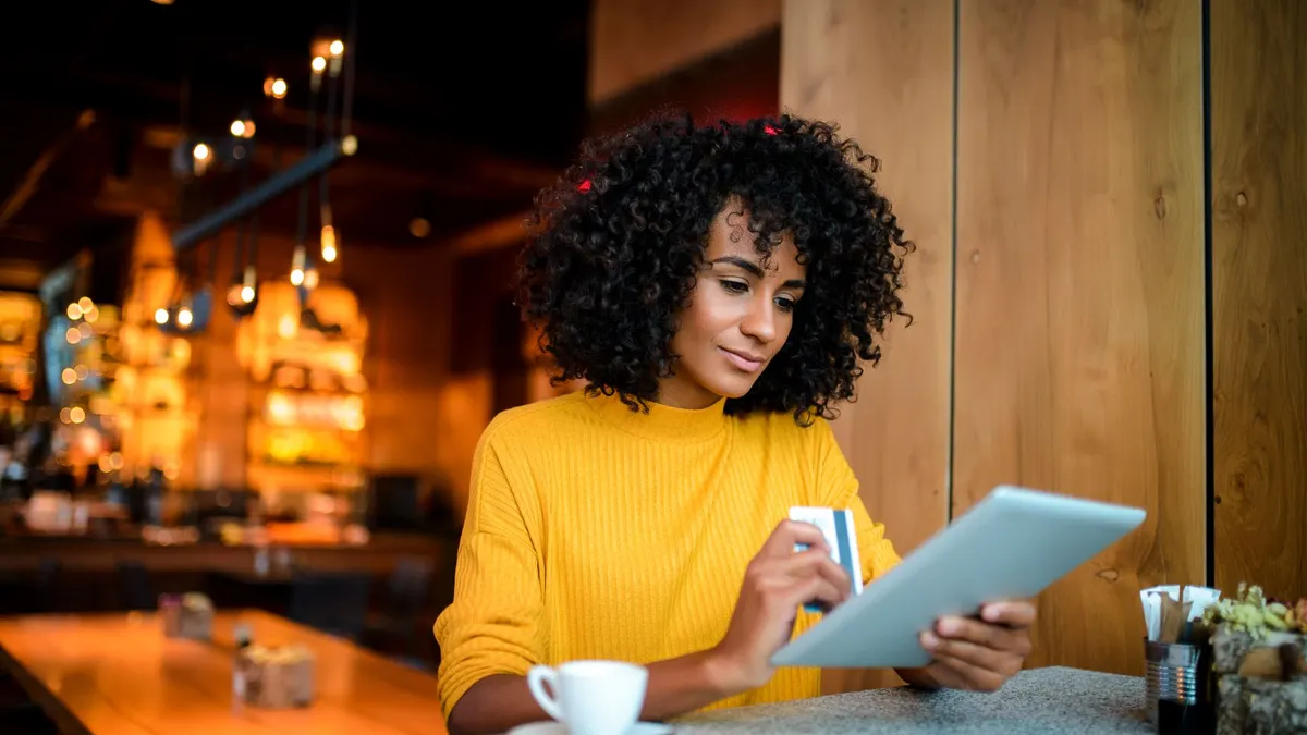 Person holding a credit card and using a tablet at a cafe