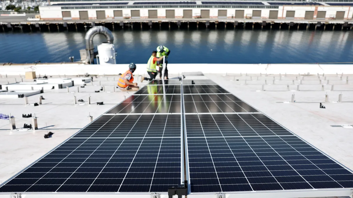 Two workers install solar panels on a roof