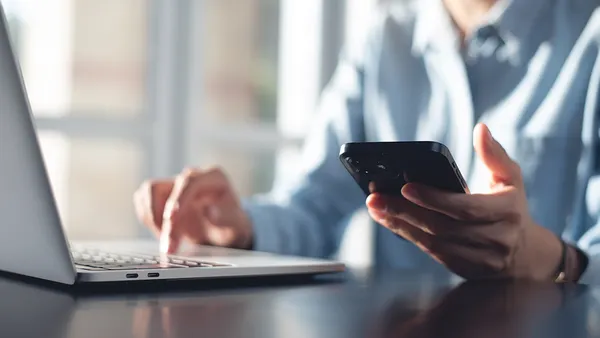 A hand with a phone in it and laptop in frame.