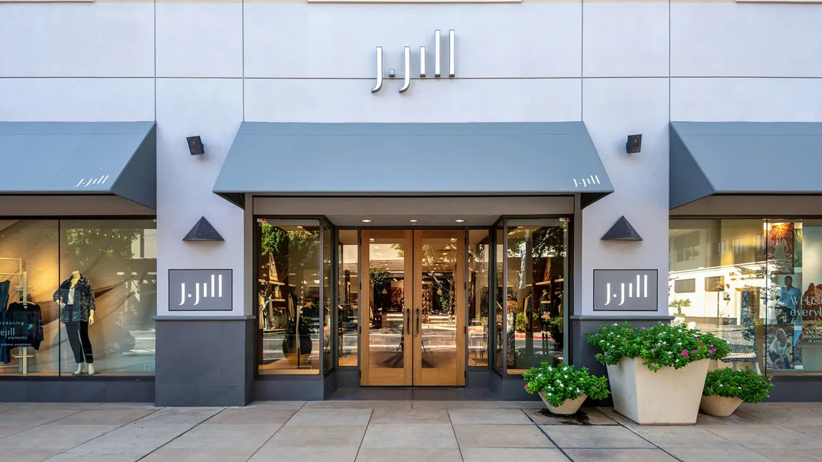 A retail store with J.Jill branding depicted from the sidewalk, featuring large planters.