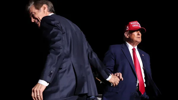 Dr. Mehmet Oz shakes hands with Donald Trump on stage against dark background