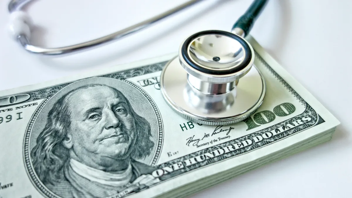 A stethoscope rests on a pile of American dollar bills.