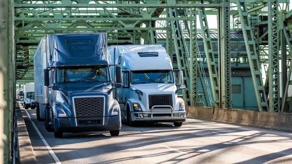 Trucks and passenger vehicles cross a bridge under metal trusses.