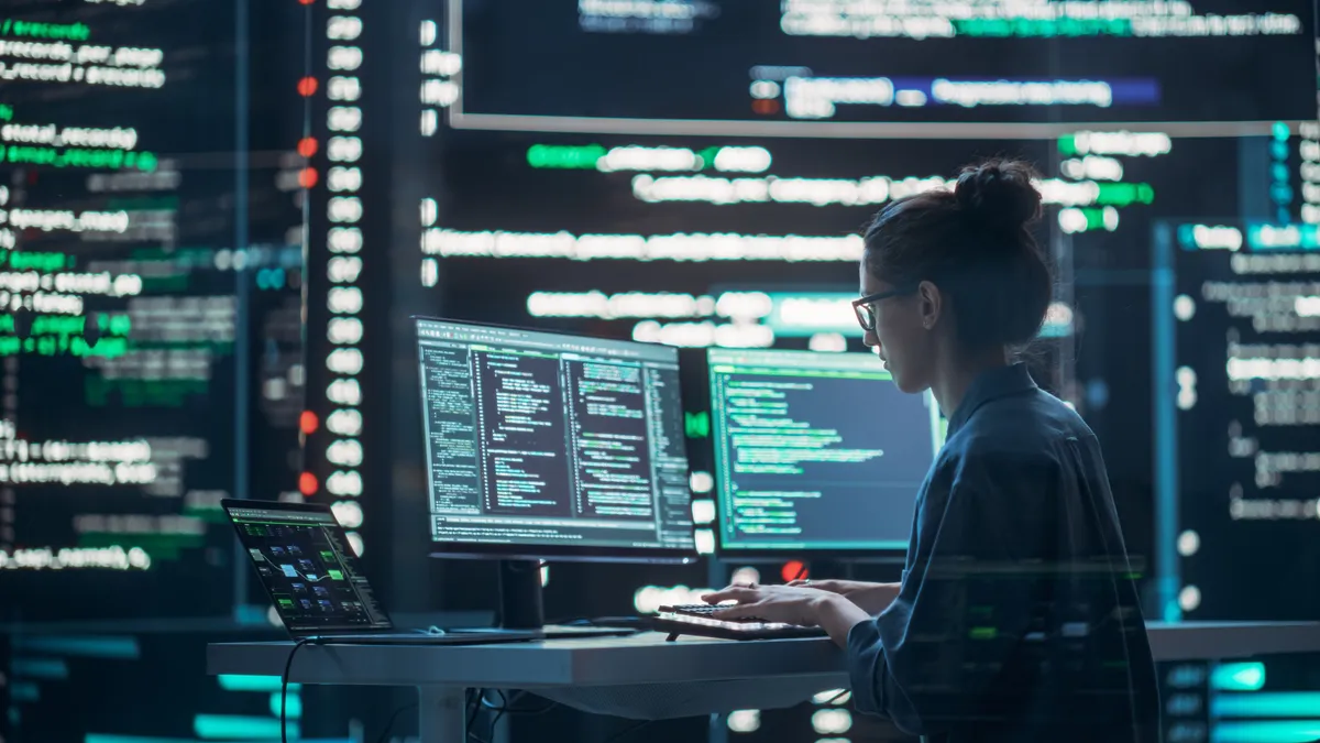 Female Developer Thinking and Typing on Computer, Surrounded by Big Screens Showing Coding Language