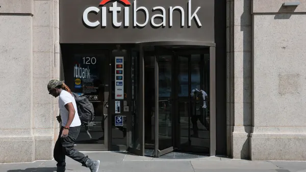 A person walks past a building entrance with "Citibank" letters above the doorway.