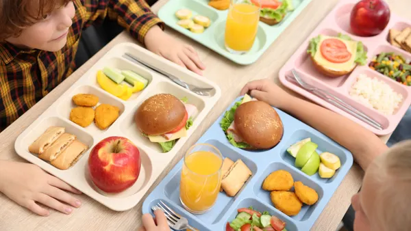 Students sit at a long table with four colorful lunch trays sitting close together.