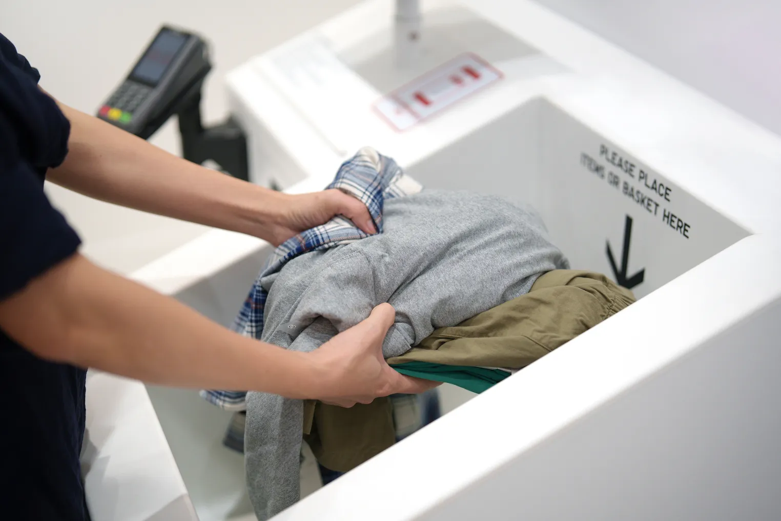 A woman puts clothing into an RFID self-checkout kiosk