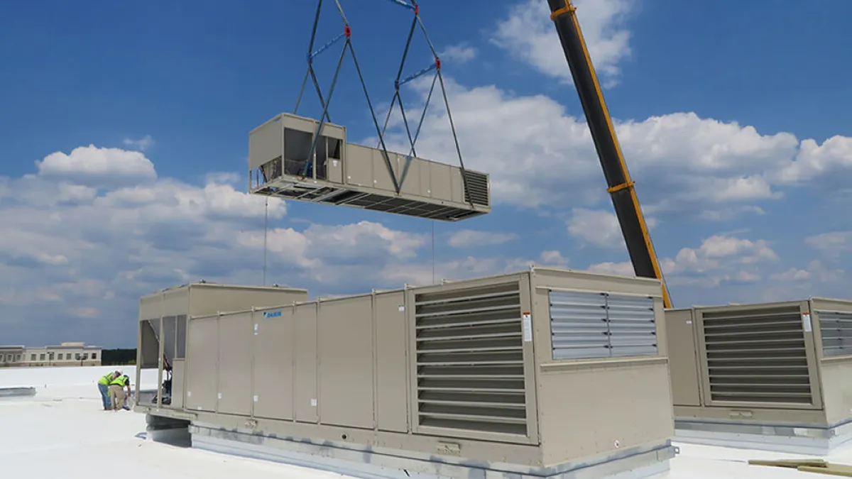 An HVAC chiller being lifted by a crane machine while another chiller is on the roof.