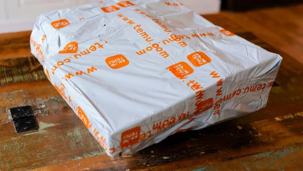 A white plastic shipping package from Temu with orange branding and website text, placed on a rustic wooden table indoors.