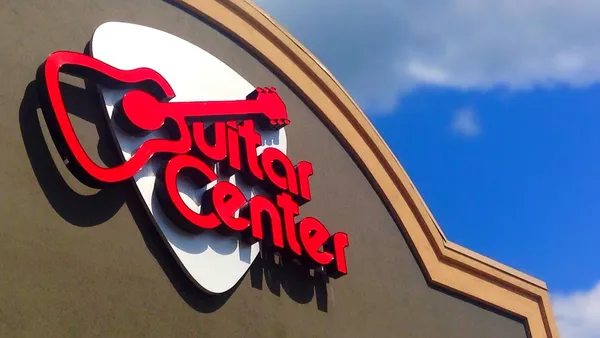 A Guitar Center signage hangs outside a storefront against a blue sky backdrop