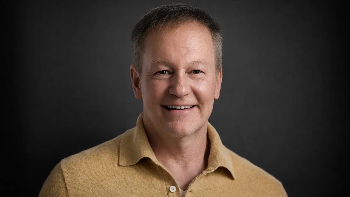 A head and shoulders photo of a person in a yellow shirt against a dark background.