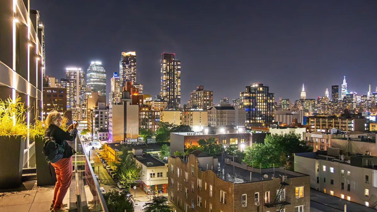 A person stands on a walkway taking a photo of a cityscape.