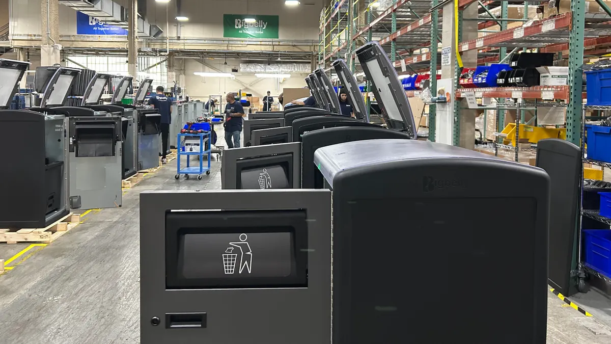 A row of partially assembled trash and recycling bins in a warehouse