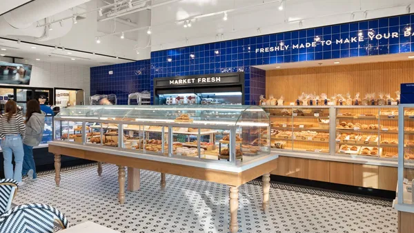 An image of inside a Paris Baguette with a display case in the foreground and breads and a refrigerated case in the background.