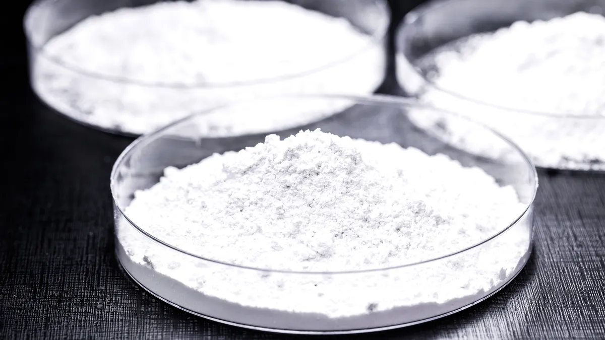 Three petri dishes of white powder set on a black table.