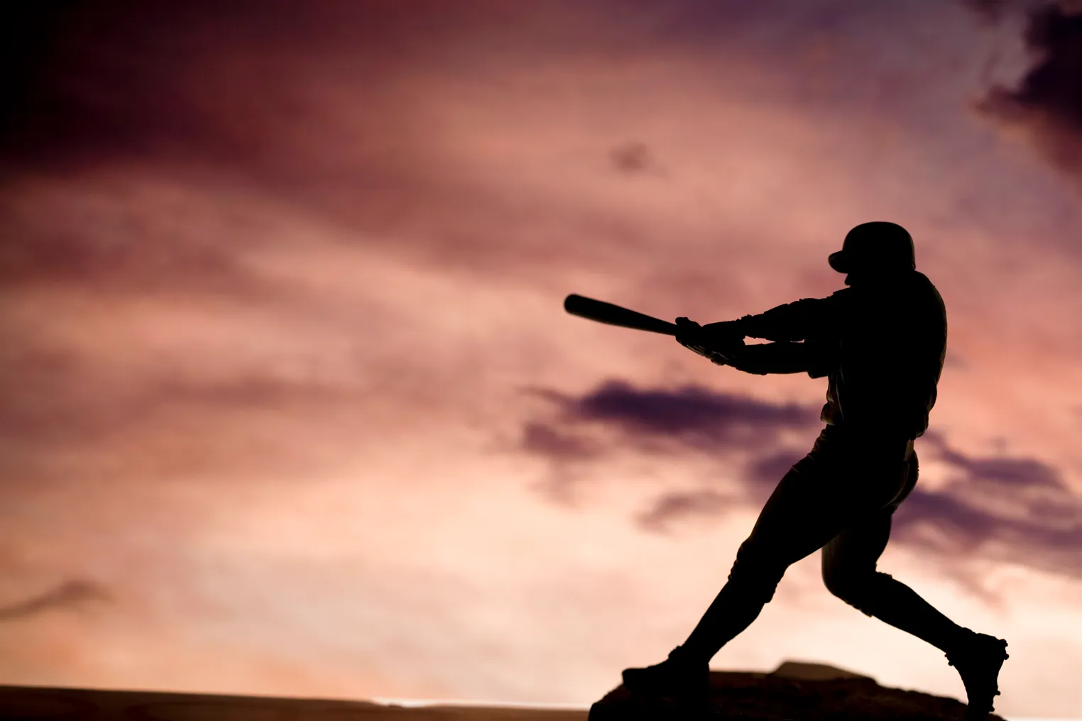 Silhouette shot of baseball player swinging a bat, hitting in the direction of clouds in the sky.