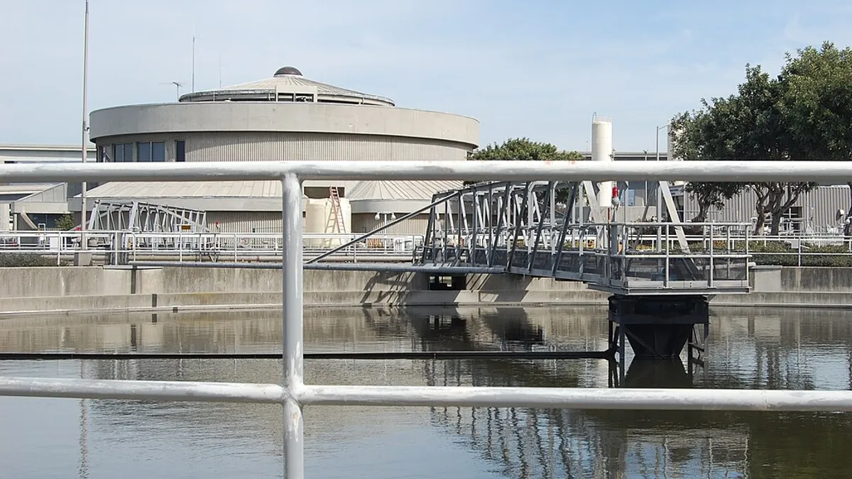 A round industrial building behind a pool of water with a walkway over top