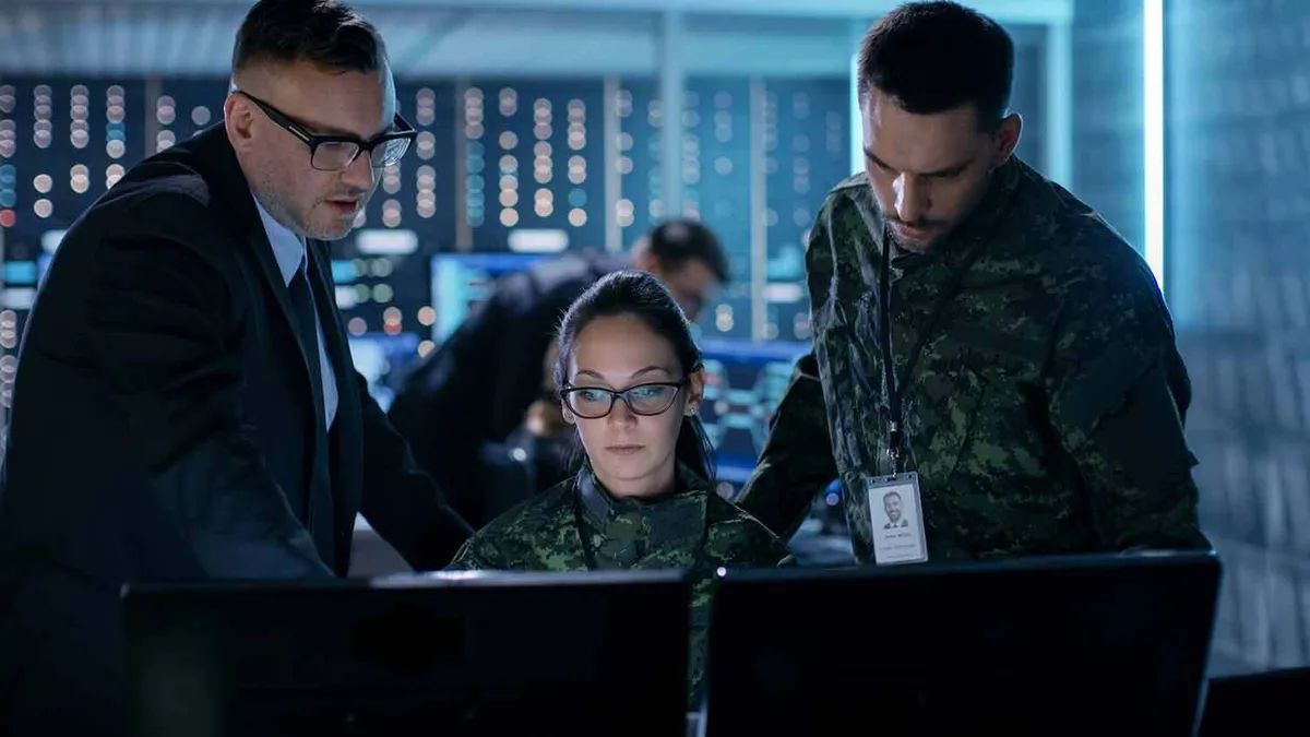 Team in military uniforms and formal attire works in a high-tech command center on computer screens.