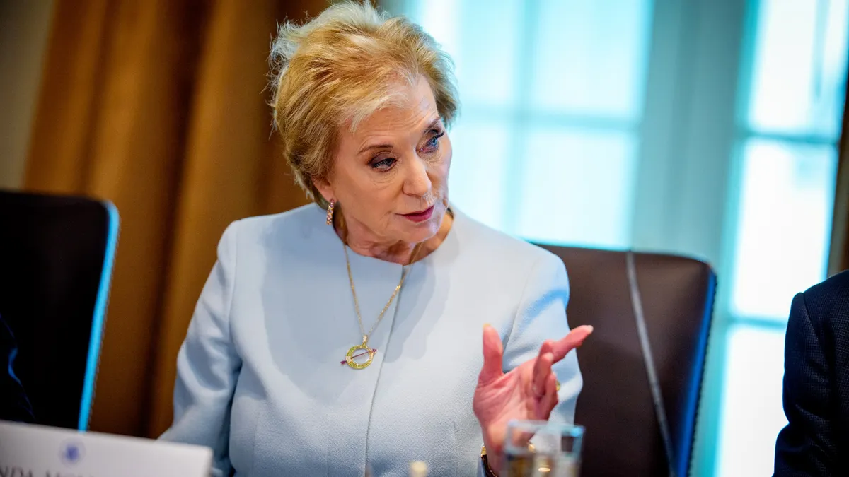 A person is sitting at a desk in a room. They are looking and pointing to their left.