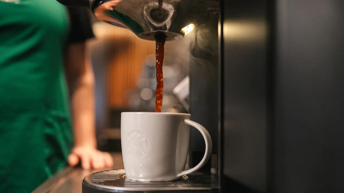 Coffee drips into a white ceramic mug emblazoned with the Starbucks logo