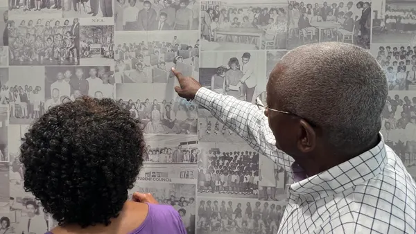 A person stands next to someone while pointing to one of the many black-and-white photos displayed on a wall.