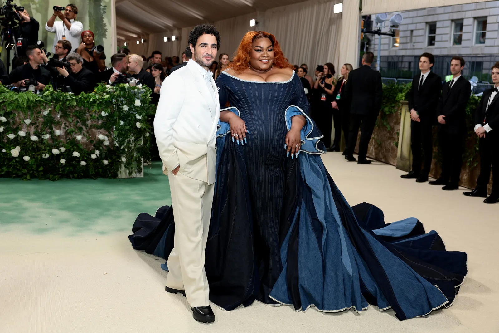 A man in a white suit and a woman in a blue denim gown stand in front of photographers.