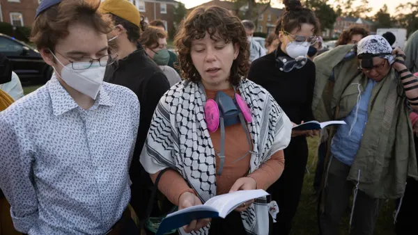 Two people, one wearing a mask, looking at an open book amid a crowd.