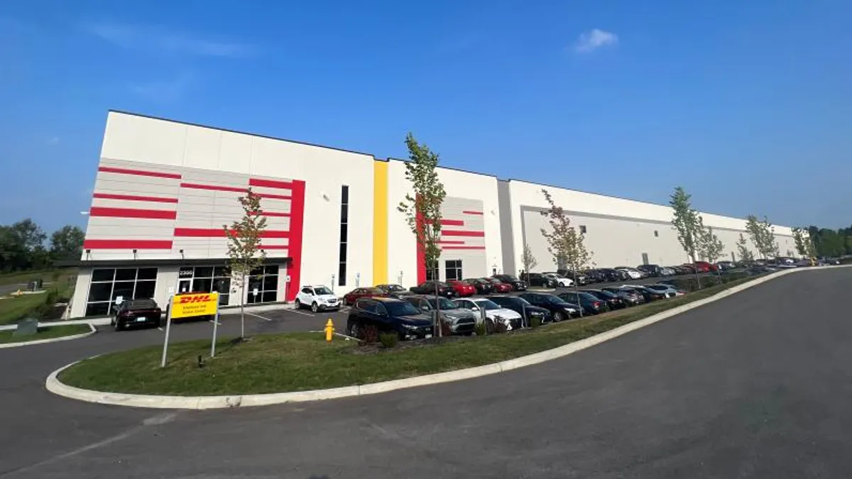 front image of a DHL eCommerce distribution facility near CVG airport, with a parking lot and parked cars in the forefront.