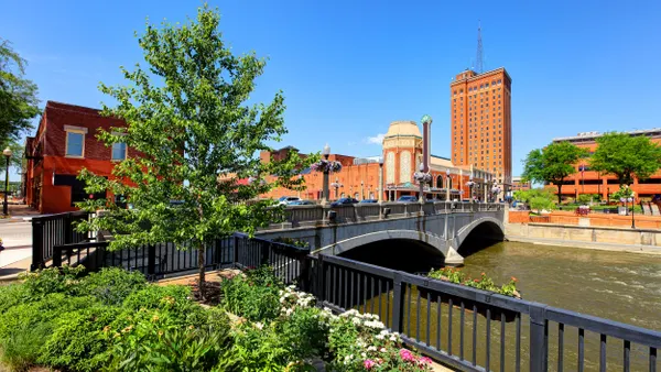 Water flows under a bridge with brick buildings and blue sky in the background.