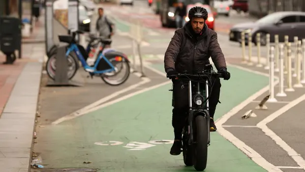 Man in heavy jacket with helmet rides an electric bike toward the camera on a green bike path.