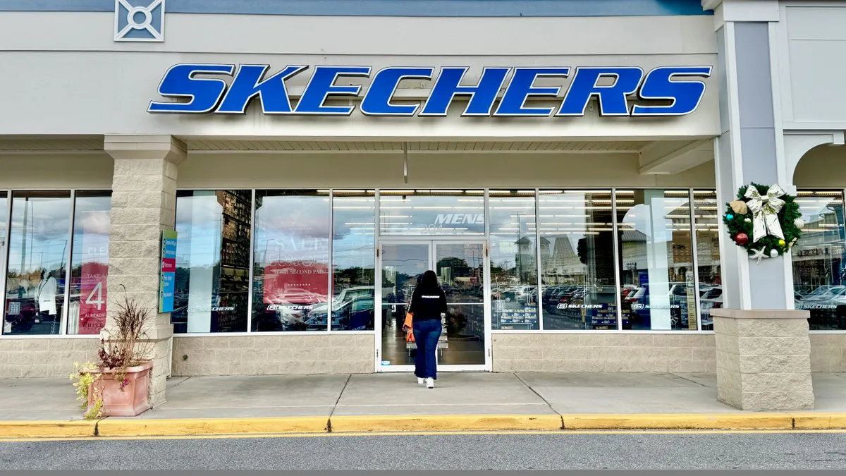 A Skechers storefront in an outdoor mall. A shopper walks into the door.