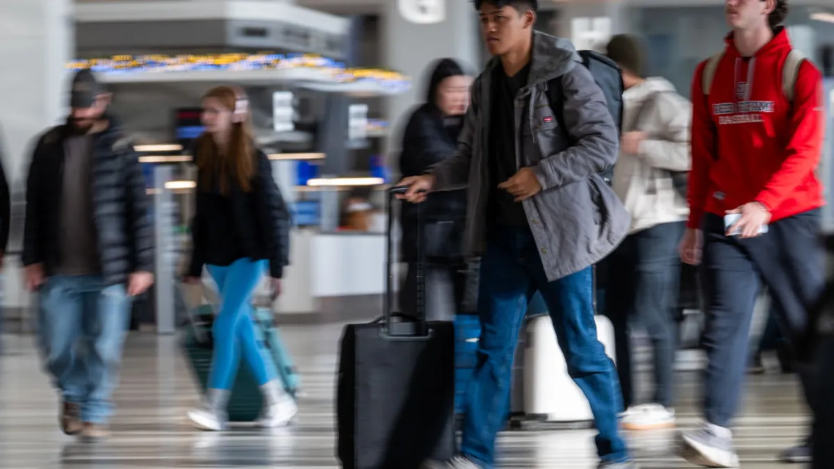 A person pushes a rolling suitcase through a busy airport.