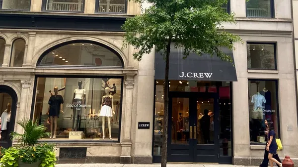 People walking past a clothing store. A tree in front of the main entrance.