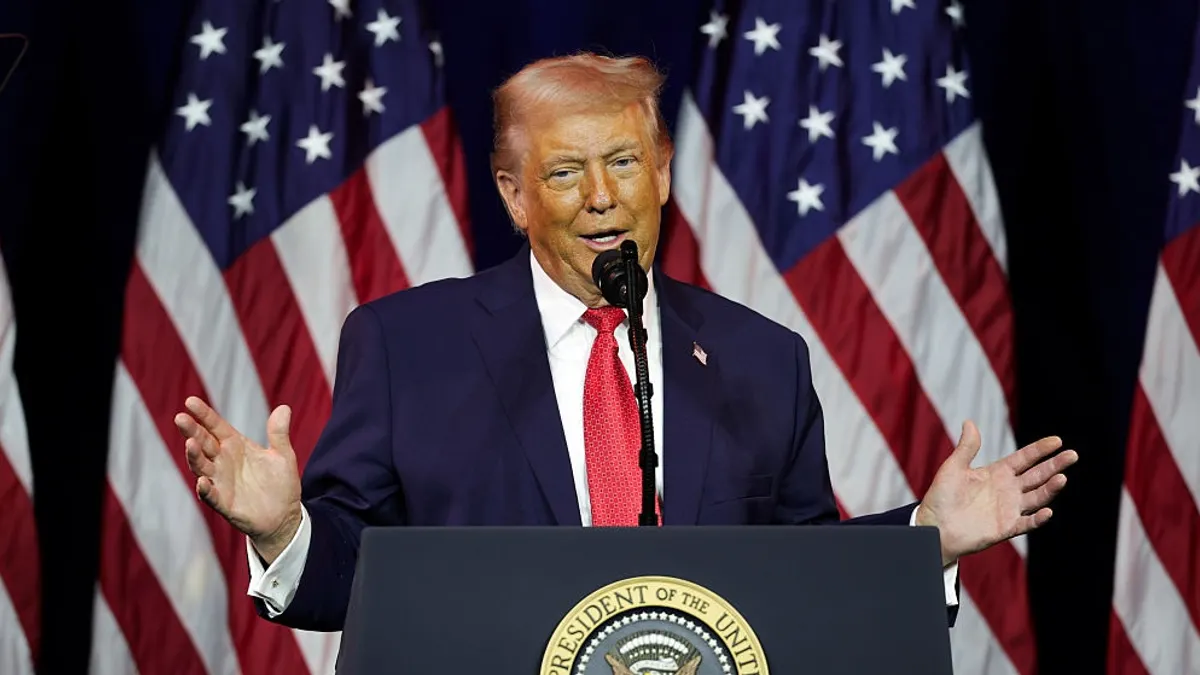 Trump stands at a podium with American flags in the background.