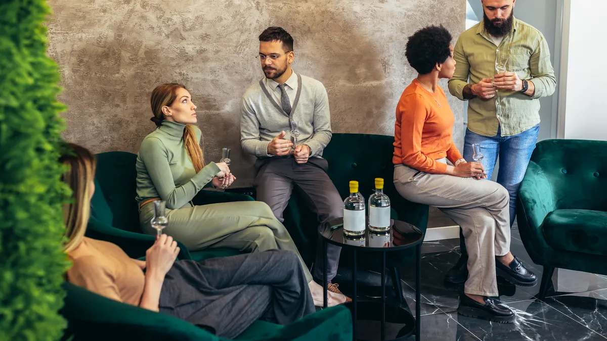 Group of businesspeople sitting together in a co-working space and celebrating with alcoholic drinks