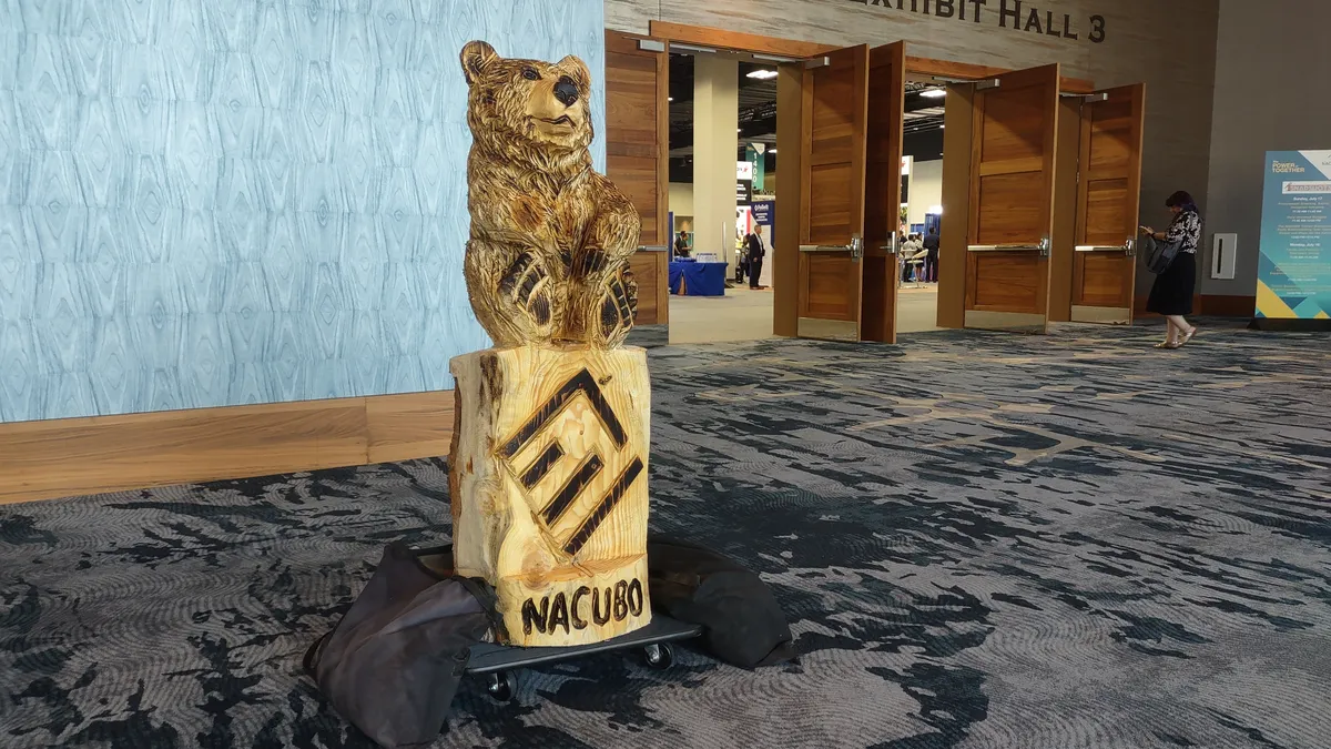 A carved wooden statue of a bear sits on top of the NACUBO logo.