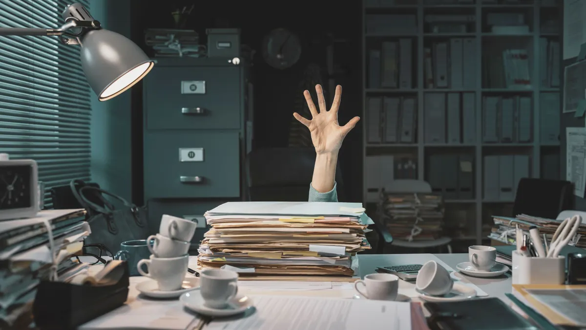 Desperate office worker overwhelmed with paperwork raising a hand to ask for help