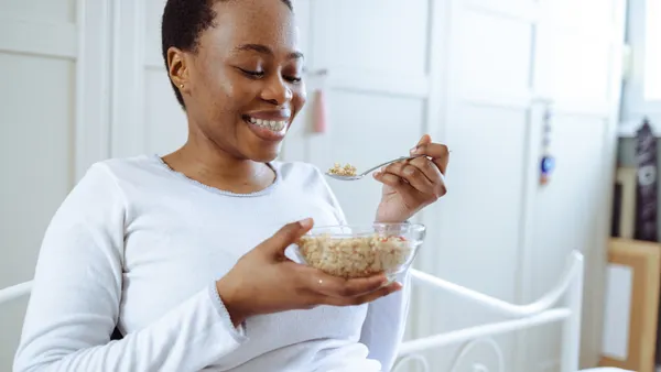 Cheerful young woman in pajamas eating cereals in bedroom