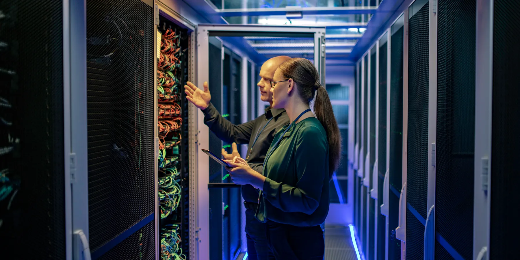 Side view of a man and a woman talking about a server in a data center while looking at it's network connection cables