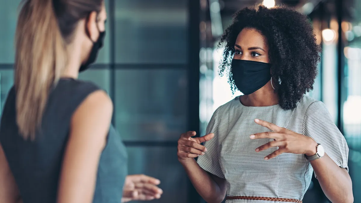 Businesswoman, wearing a mask, standing at distance and talking to a colleague.