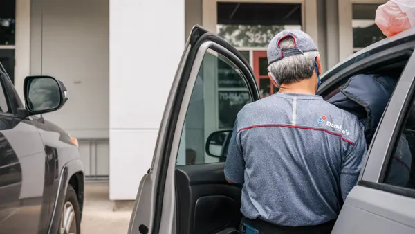 A Domino's worker loads an order into a car.