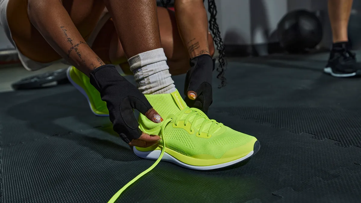 Someone ties the laces of Lululemon's yellow Chargefeel cross-training shoe.