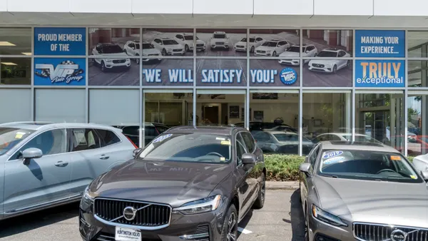 Three vehicles sit in front of a dealership, with signs that say "Proud Member of the VIP Auto Group," "We Will Satisfy You!" and "Making Your Experience... Truly Exceptional! plastered on the windows.