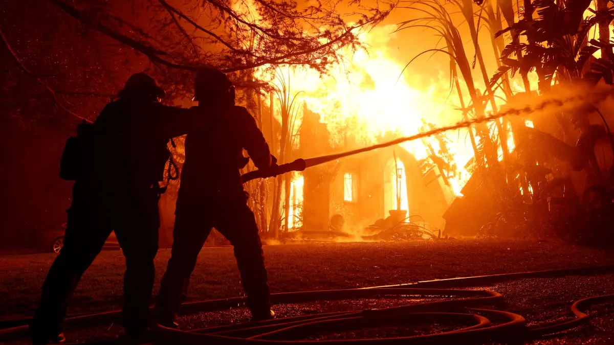 A pair of firefighters spray water on a burning home